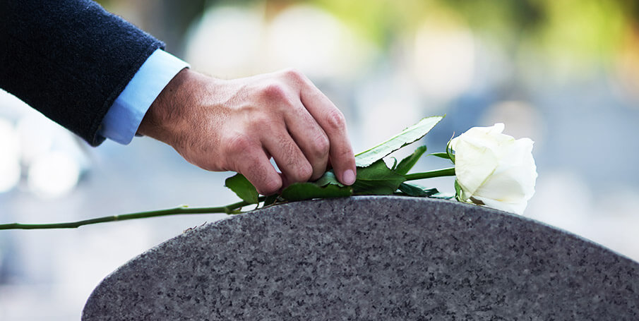 man placing white rose on a gravestone 